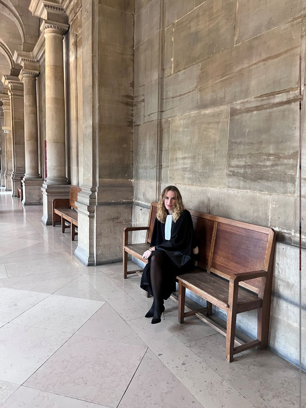 Maître Mélodie Brun en robe d'avocate, assise sous la galerie à colonnes d'un palais de justice